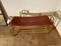 Full view of decorative brass bench showing brown upholstered seat and brass frame on carpeted flooring.