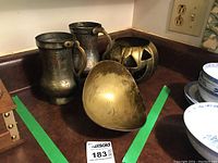 Full view of brass pumpkin, two mugs, and bowl arranged on a countertop