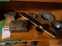 Photo showing the brass telescope and various brass containers, boxes, bowls, and trays arranged on a wooden shelf.