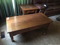 Photo of the oak coffee table and matching side table placed next to a brown leather sofa showing overall design and condition including drawers and legs.