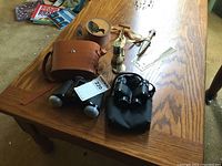 Overview of lot displaying binoculars with cases, leather jar, shaving set, whistle, dagger and bookmark on wooden table