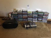 Sony portable radio and large stack of music CDs on floor next to wall with electrical outlet.