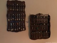 Two wooden wall racks mounted and holding multiple rows of collector spoons representing various regions and themes.