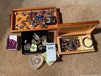 Overview of three wooden boxes containing rings, brooches, pins; white box with purple beads; black box with brooches; clear glass dish on carpet