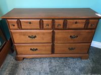 Front view of maple dresser showing 6 drawers with metal hardware, medium brown finish, and shaped base detail.
