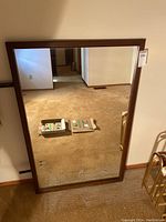Front view of a large rectangular dresser mirror with wooden frame, reflecting a room with beige carpet and white walls.