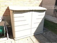Front exterior view of closed storage box against brick wall showing overall shape and color