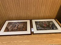 Two framed Indonesian art prints placed side by side on a wooden floor against a wall. Both prints are signed limited editions measuring 13x19 inches.