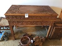 Full frontal photo of the ornately carved wooden table with carved floral decorations and removable top.