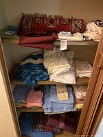 Shelf filled with folded bed linens, blankets, doilies, towels, and face-cloths in various colors and patterns.