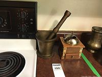 Brass mortar and pestle beside a wooden manual coffee grinder placed on a kitchen counter next to a stovetop.