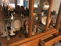 Wide view of wooden cabinet shelves filled with various souvenir figurines including carved animals, vases, plates, and abstract sculptures.