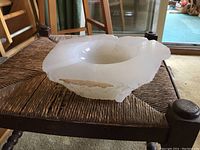 Large white marble ashtray showing chip on edge, placed on woven chair seat