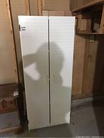 Front view of white utility cabinet showing closed double doors with pull handles.