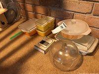 Photo showing four vintage Pyrex casserole dishes with lids, two small yellow, one medium yellow, and one large orange, plus clear glass casseroles and rose bowl with lid