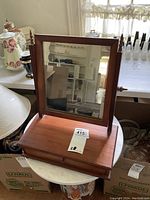 Front view of the antique wooden shaving mirror with a rectangular adjustable mirror and wooden supports on a table.