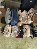 Overview of 12 bags and purses displayed on floor showing different sizes, colors and styles including beige large tote, blue small bag, and structured beige bags.