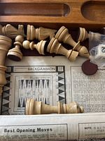 Close-up of cream light colored wooden chess pieces, partial backgammon board instructions and dice in plastic bag.