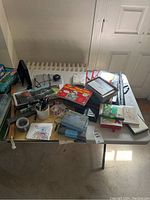 Top view of table with various office supplies and desk items scattered on it including books, tape, stamps, trays, and papers.