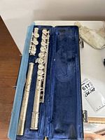 Open blue velvet-lined hard case showing disassembled flute pieces: headjoint, body, and footjoint laid out inside.