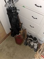 Lot contents showing black Knight golf bag holding Spaulding Century Series golf clubs, wooden tennis rackets, two pairs of ice skates on floor.