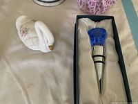 Blue diamond-shaped glass wine stopper in box and white ceramic swan with floral detail.
