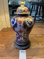 Front view of the lamp body detailing the Japanese Imari style hand-painted porcelain with floral and bird motifs in blue, red, and gold. Wooden base is visible with some wear.