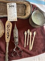 Photo showing metal candle wick cutters with ornate handle, pierced cake server and small silver spoons.