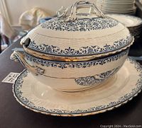 Side view of covered tureen atop matching platter showing blue floral pattern and gold trim
