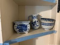 Photo of four pieces of Polish blue and white china displayed on a shelf, includes a footed planter, water pitcher, and two bowls stacked