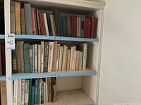 Shelf with a variety of classic and vintage hardcover and paperback books arranged upright with some wear visible.