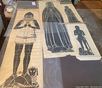Wide shot showing four large handmade medieval brass rubbings laid out on table, depicting armed knights and noble figures with heraldic animals.