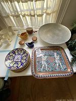 Full view of all items on table including dishes, large silver bowl, pitchers, and wall plate.