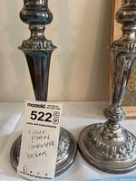 Photo of two silverplated candle stick holders showing overall design and shape with a MaxSold tag.