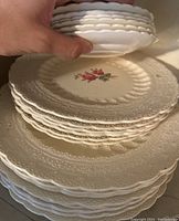 Stack of various sizes of Spode's Jewel Copeland plates with scalloped edges and rose pattern on white ceramic.