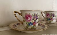 Close-up of a single tea cup and saucer showing floral and gold rim detail
