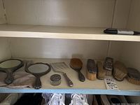 Overview of entire vanity set on shelf including two hand mirrors, comb, glass jar, and three brushes.