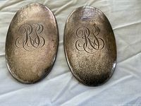 Two oval-shaped hair brush backs engraved with initials 'RS', showing patina and wear.