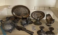 Overall view of vintage plated kitchenware items collected on a shelf, showing tea kettle, tea pot, trays, candle holders, and utensils.