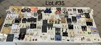 Wide view of 68 earrings laid out in rows on white surface showing various styles and brands.