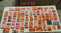 Full overview of numerous pairs of pierced earrings arranged on orange, pink, black, and purple display cards spread out on a table.