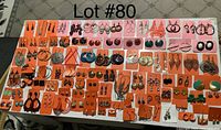 Full view of arranged earrings on a table, showing large assortment mostly on orange and pink cards.