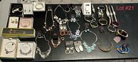 Full lot of various jewelry displayed on a black surface showing multiple necklaces, earrings, bracelets and watches