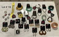 Photo showing variety of bracelets, earrings, and rings laid out on a white surface for lot overview