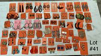 Wide view of 60 pairs of pre-owned pierced earrings displayed on orange cards, showing variety of styles and colors including hoops, studs, dangles and chandelier earrings.