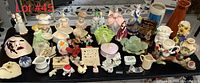 Overview of assorted vintage ceramic flower pots, lady figurines, small pitchers, and knickknacks on black table