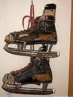 Side view of pair of heavily weathered Bauer ice skates showing cracked leather and metal blades.