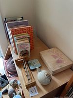 View of assorted cookbooks, wooden timer, small tins, ceramic bird figurine, and boxed item on a wooden table