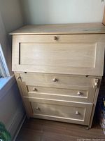 Closed view of light wood fold-down computer desk with three drawers.