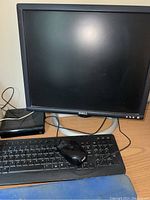 Dell monitor, keyboard, mouse and small black device on wood desk